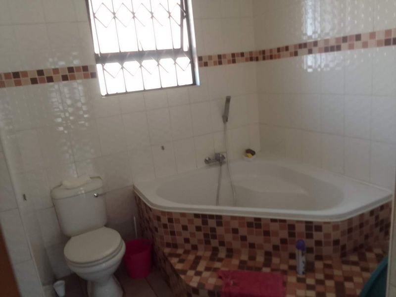 A functional bathroom featuring a corner bathtub, toilet, and tiled wall finishes with decorative accents.