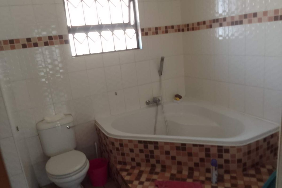 A functional bathroom featuring a corner bathtub, toilet, and tiled wall finishes with decorative accents.