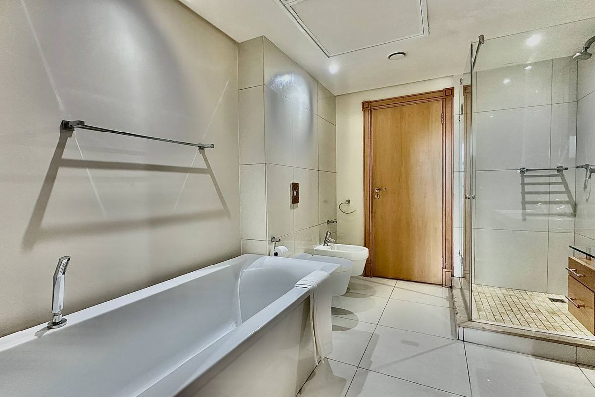 Modern bathroom featuring a white bathtub, glass-enclosed shower, bidet, and wall-mounted vanity with neutral floor-to-ceiling tiling.