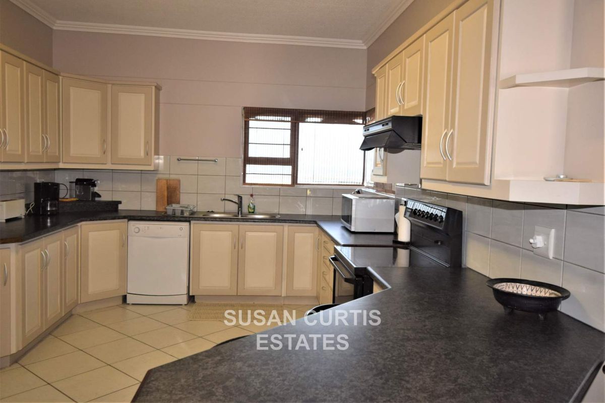 A functional kitchen featuring cream-toned cabinetry, dark laminate countertops, tiled splashbacks, and a built-in extractor fan.