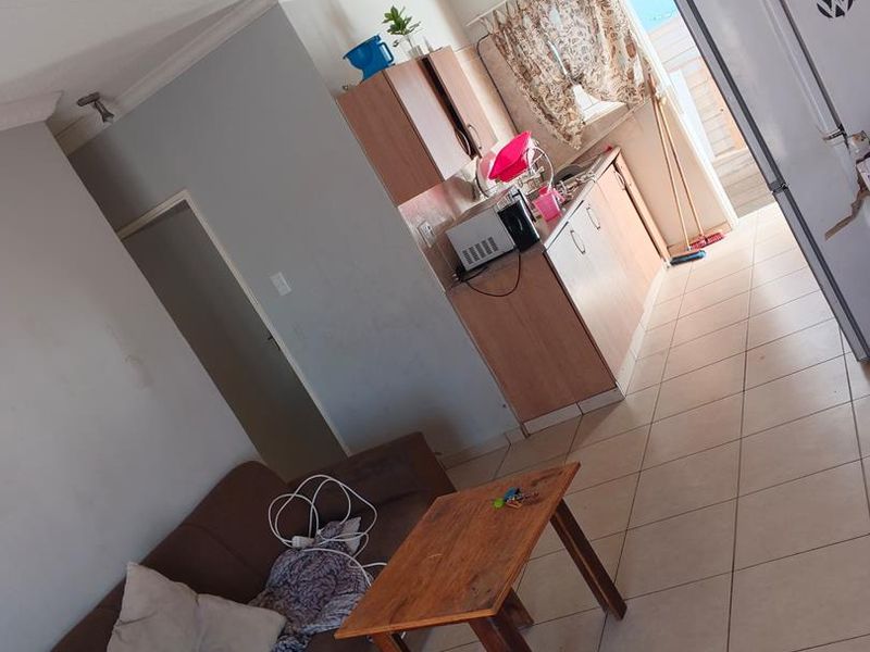 Open-plan living and kitchen area featuring tiled flooring, built-in cabinetry, and coved ceilings, offering a functional layout in need of cosmetic updates.