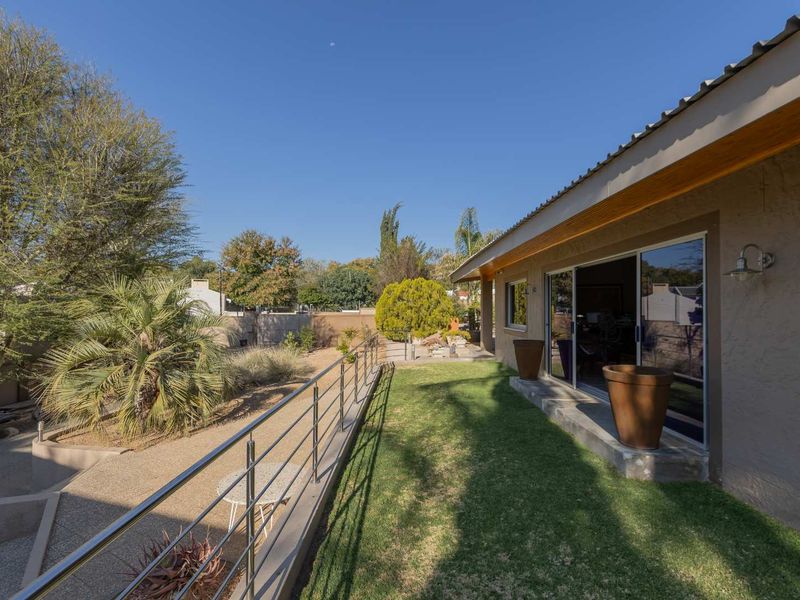 A well-maintained rear exterior featuring a manicured lawn, a concrete patio area with a stainless steel balustrade, and sliding glass door access.
