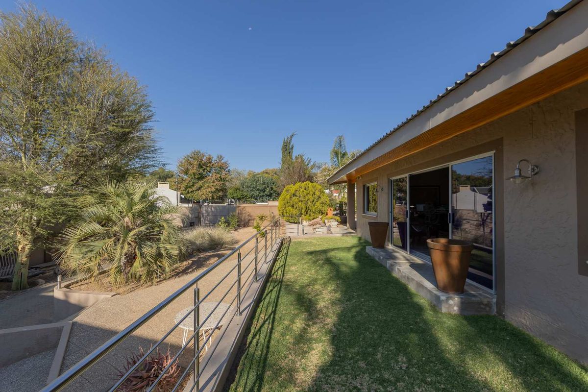A well-maintained rear exterior featuring a manicured lawn, a concrete patio area with a stainless steel balustrade, and sliding glass door access.