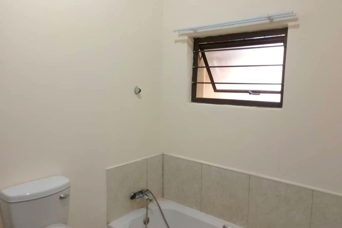 A functional bathroom featuring a standard bathtub with a handheld shower mixer, a toilet, and a window with security bars.