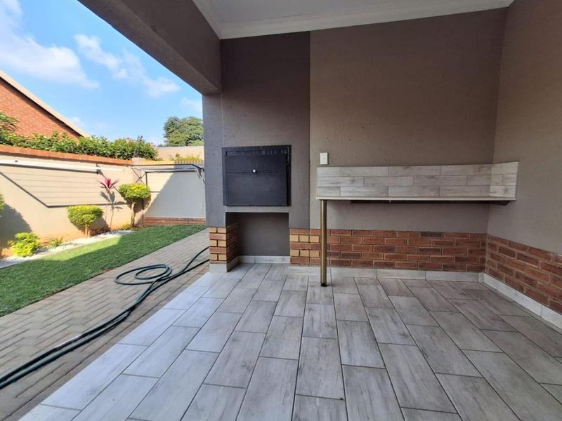 Covered patio area featuring a built-in braai, tiled flooring, and a brick-accented counter, overlooking a private garden space.