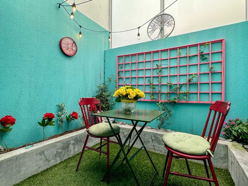 A compact outdoor patio area featuring a raised concrete planter bed, decorative wall trellis, and ambient string lighting, creating a cozy entertainment space.