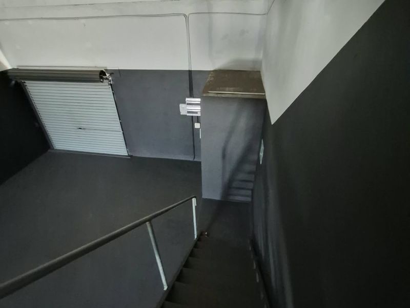 Industrial utility space featuring a staircase, roller shutter door, and exposed timber ceiling beams with a modern dark grey finish.