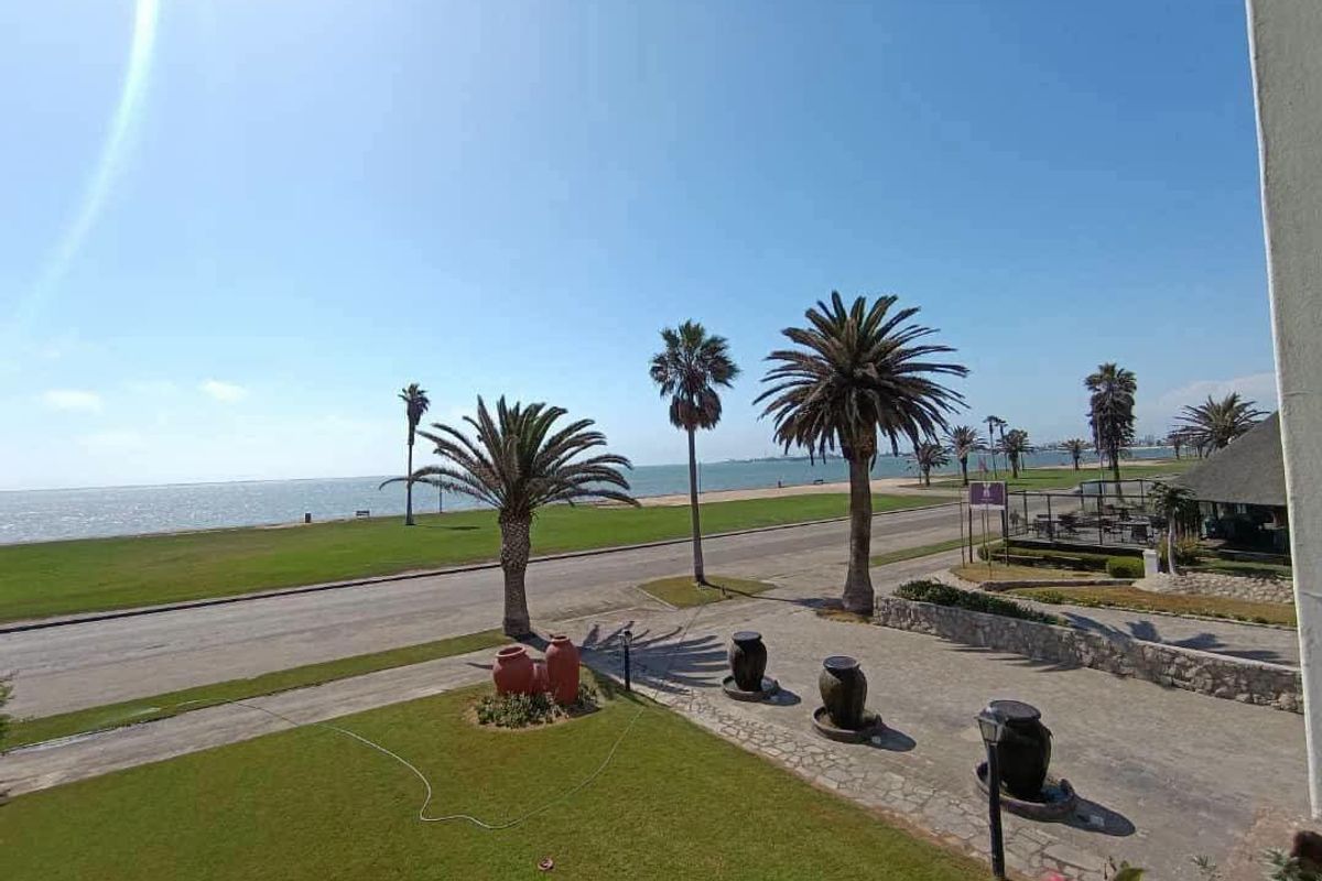 Elevated view overlooking a coastal road, landscaped garden, and the ocean beyond.