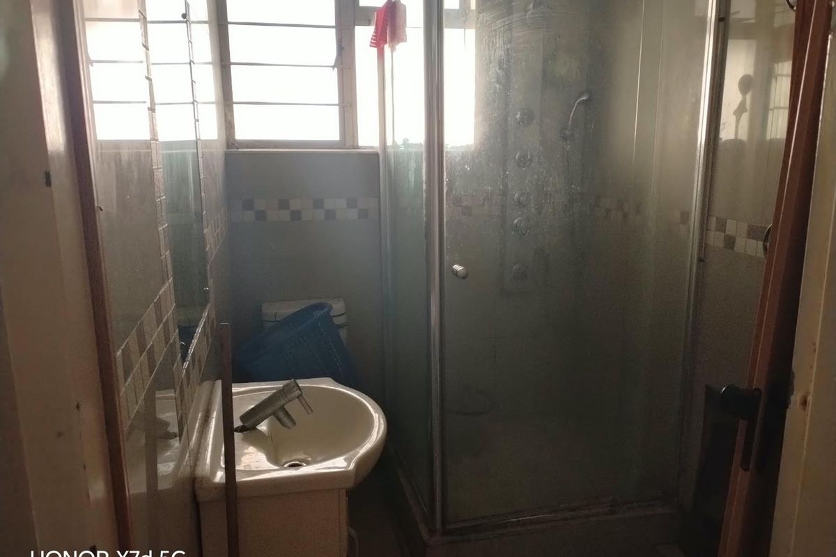 A compact bathroom featuring a shower enclosure, wall-mounted basin, and toilet, with tiled walls and a window providing natural light.