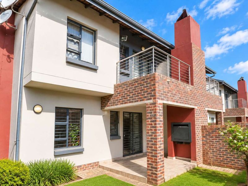Rear view of a double-story townhouse featuring a covered patio with a built-in braai, a balcony, and a private garden area.