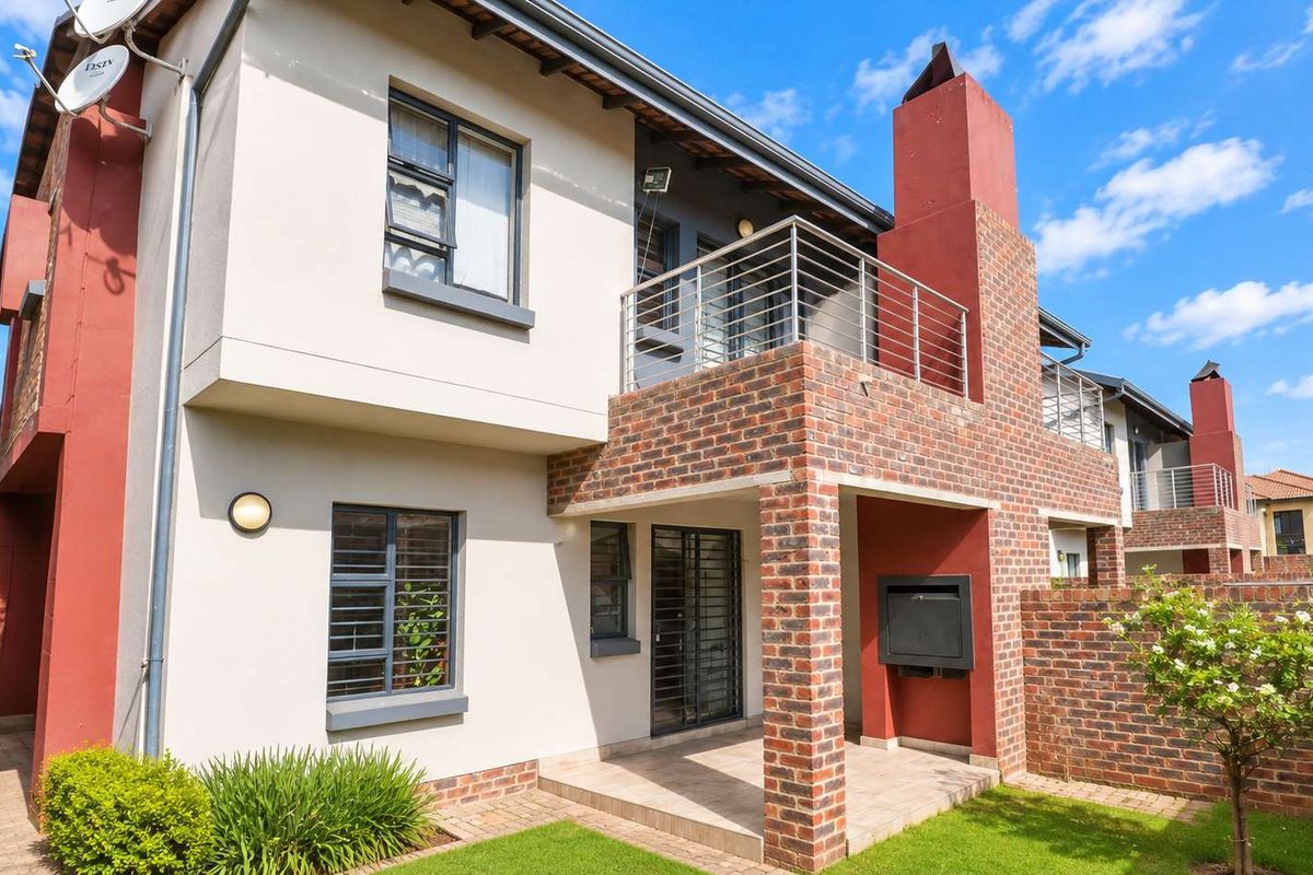 Rear view of a double-story townhouse featuring a covered patio with a built-in braai, a balcony, and a private garden area.