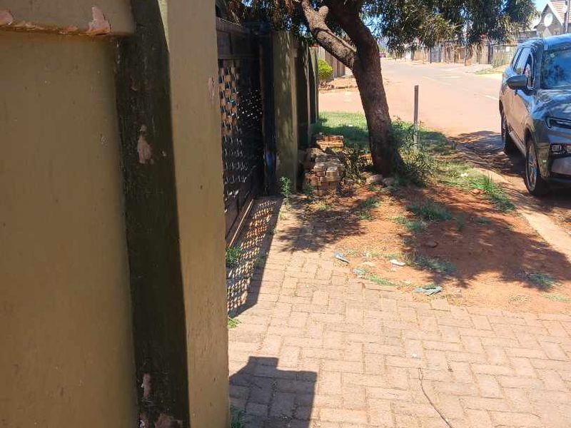 Street view showing the property boundary wall, metal gate, and paved driveway area with visible wear to the exterior wall finish.