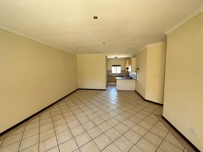 An open-plan living and kitchen area featuring neutral wall tones and tiled flooring, offering a blank canvas for interior design.