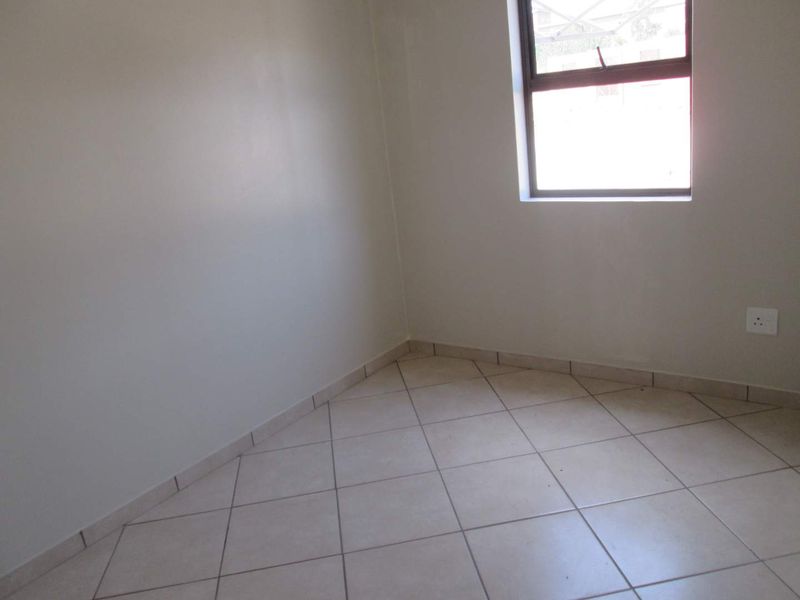 A clean, empty bedroom featuring neutral tiled flooring, plain walls, and a window providing natural light.