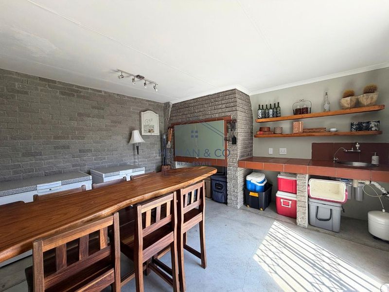 Covered patio area featuring a built-in braai, tiled prep counter with sink, and exposed brick wall detailing.