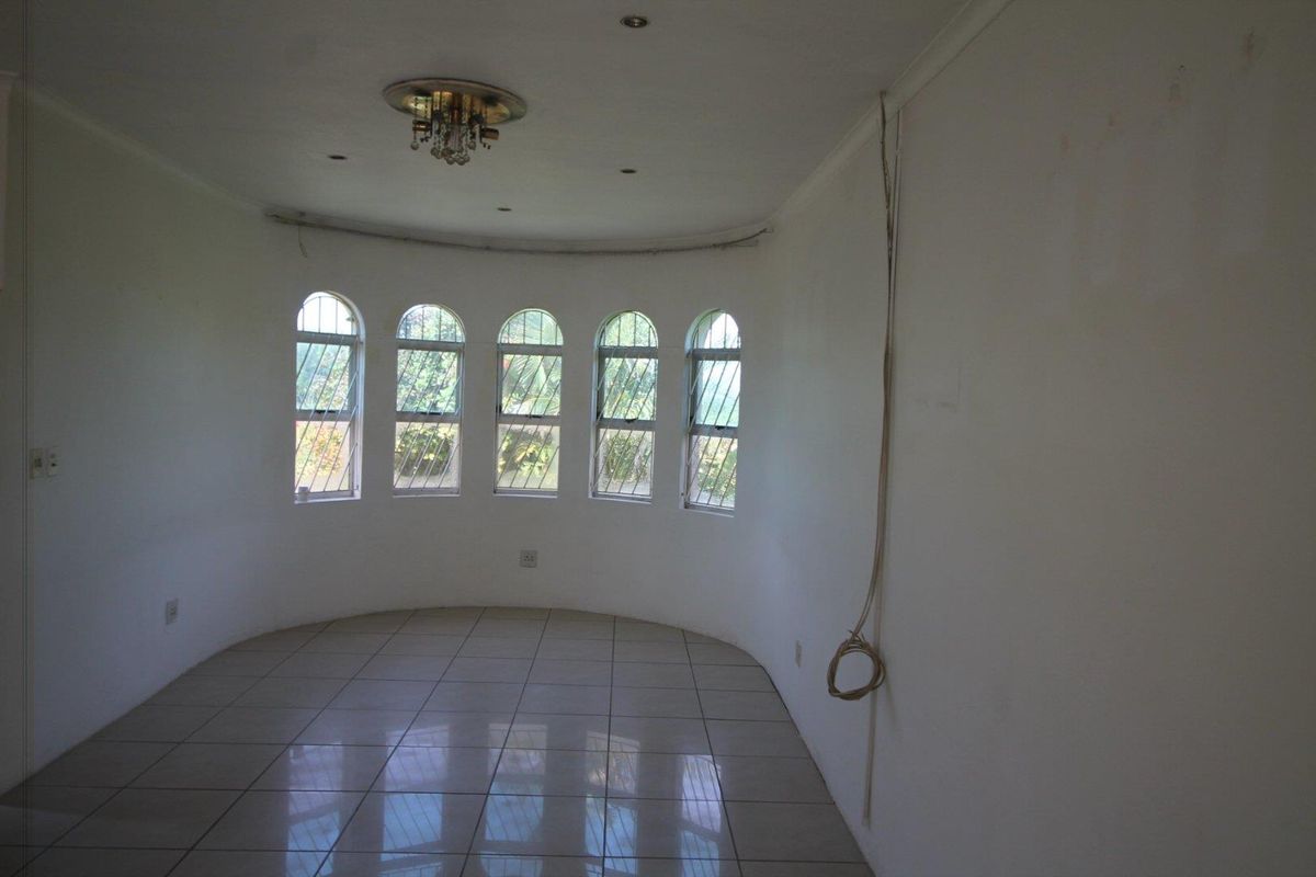 An empty, curved-wall living area featuring tiled flooring, arched windows with security bars, and a central chandelier.