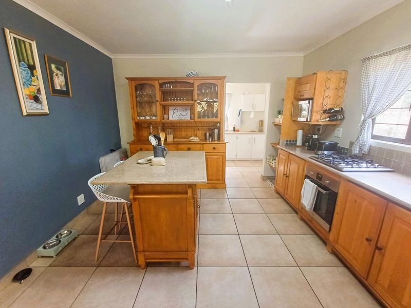 A functional kitchen featuring wooden cabinetry, stone countertops, a gas hob, and an integrated oven, with an adjoining scullery area and tiled flooring.