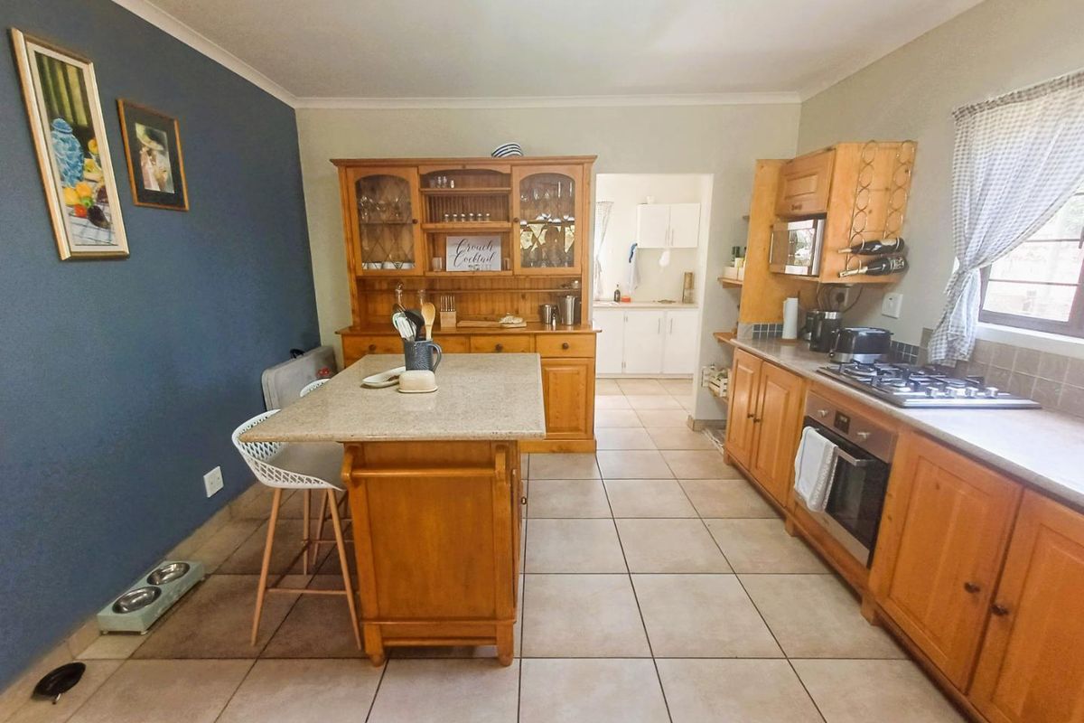 A functional kitchen featuring wooden cabinetry, stone countertops, a gas hob, and an integrated oven, with an adjoining scullery area and tiled flooring.
