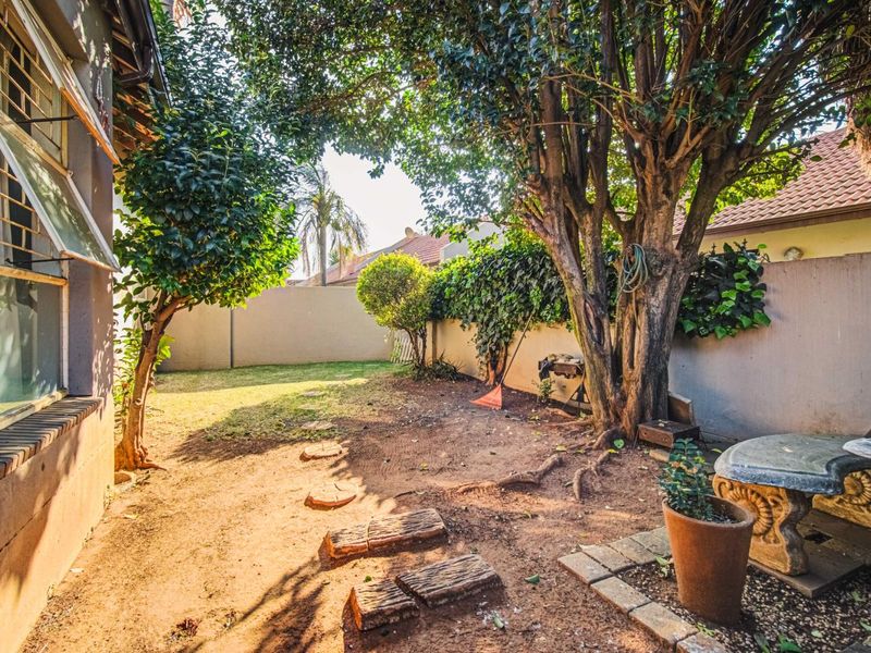 A private rear garden area featuring mature trees, perimeter walling, and a small paved section adjacent to the townhouse exterior.