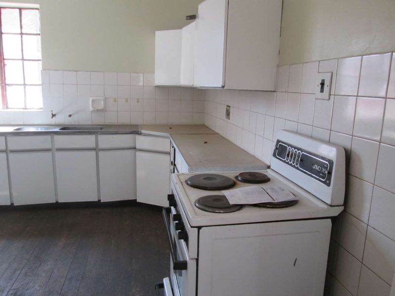 A dated kitchen featuring original cabinetry, a tiled backsplash, and a freestanding electric stove, offering significant potential for modernization and renovation.