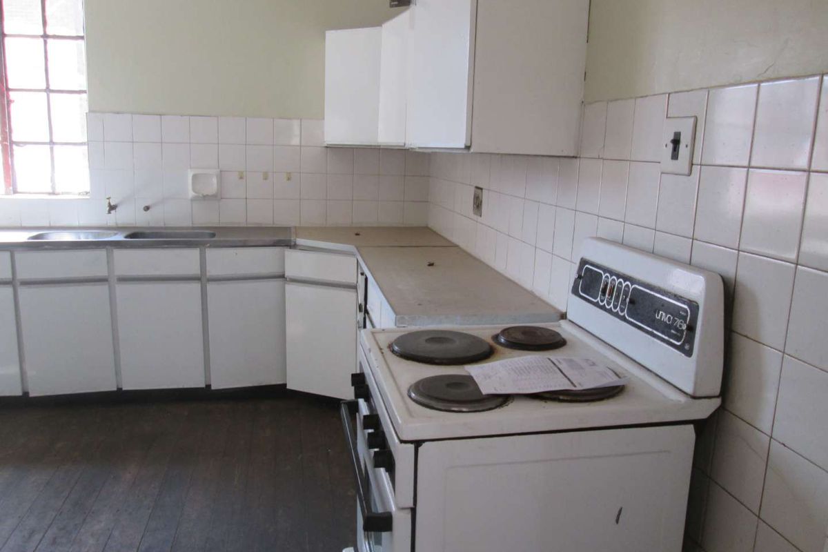 A dated kitchen featuring original cabinetry, a tiled backsplash, and a freestanding electric stove, offering significant potential for modernization and renovation.