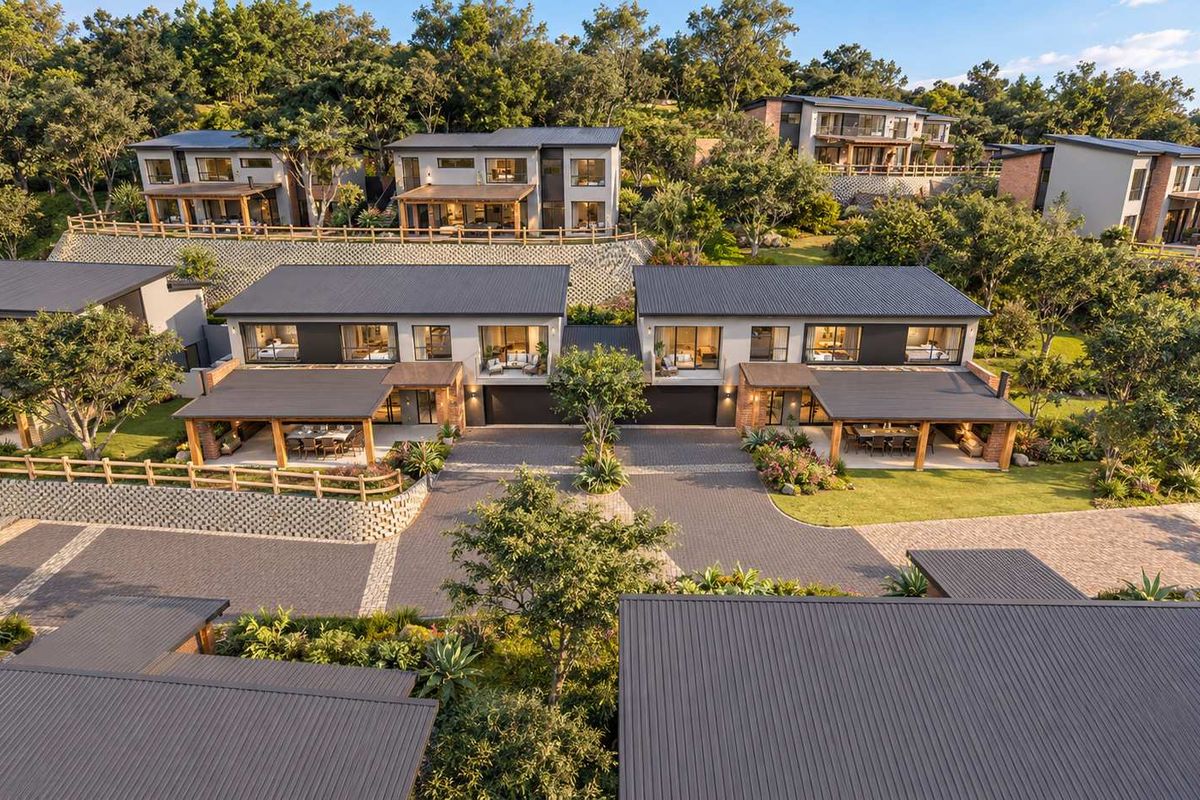 Aerial view of a modern townhouse complex featuring paved driveways, covered patios, and landscaped gardens set against a hillside backdrop.