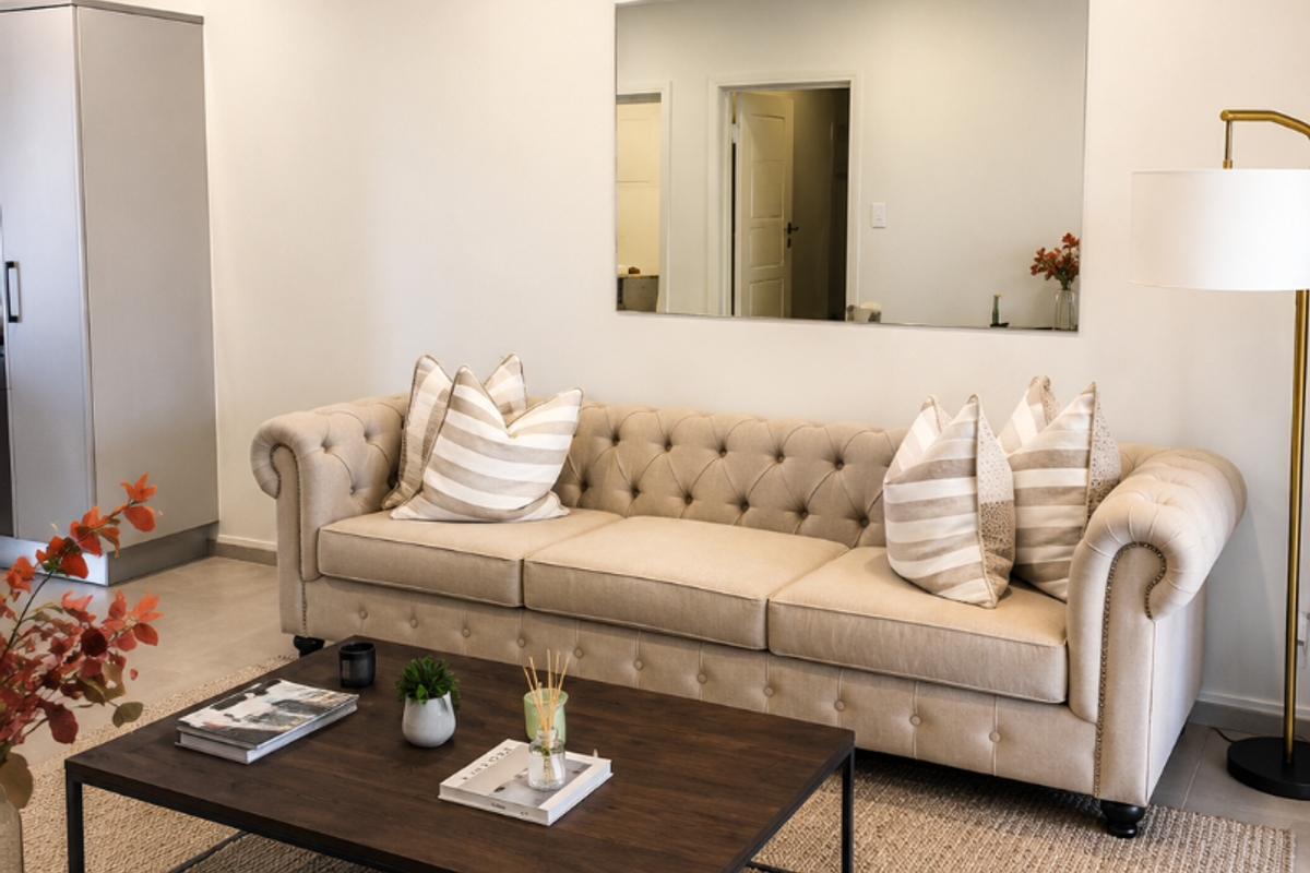 A well-maintained living room featuring neutral tiled flooring, recessed downlighting, and a large wall-mounted mirror, creating a bright and inviting space.