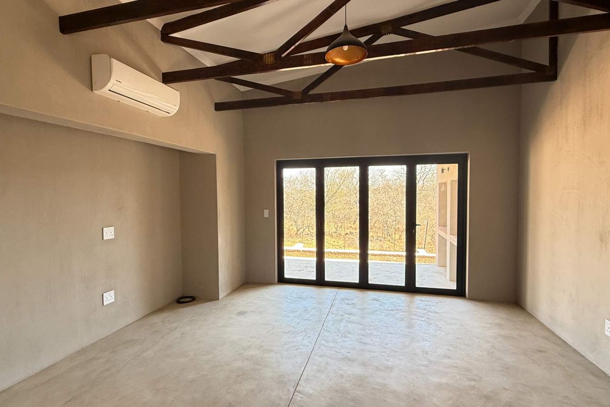 Spacious living area featuring exposed timber roof trusses, polished concrete flooring, and large glass sliding doors opening to an outdoor patio.