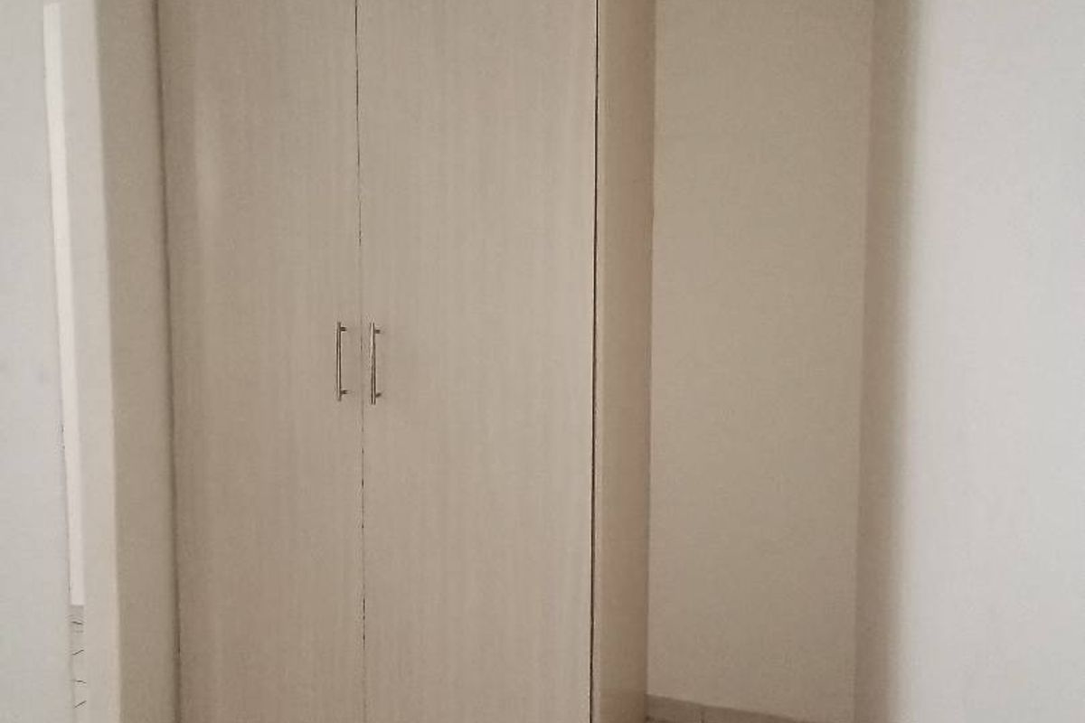 A simple bedroom space featuring neutral tiled flooring and a functional built-in wardrobe with light wood-finish doors.