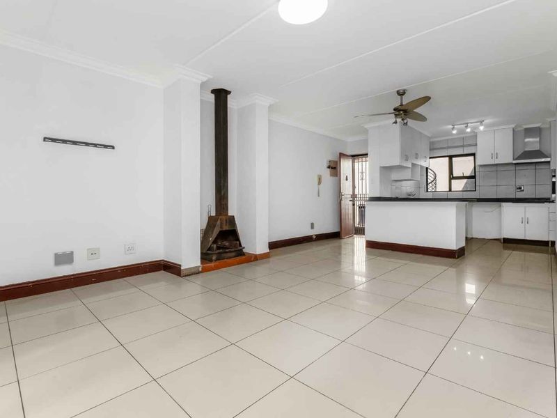 Spacious open-plan living area featuring tiled floors, a central fireplace, and a functional kitchen with breakfast bar and built-in cabinetry.