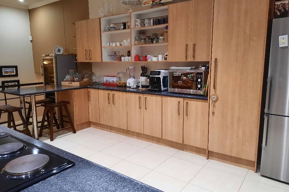 A functional kitchen featuring light wood cabinetry, dark granite countertops, a breakfast bar, and tiled flooring.