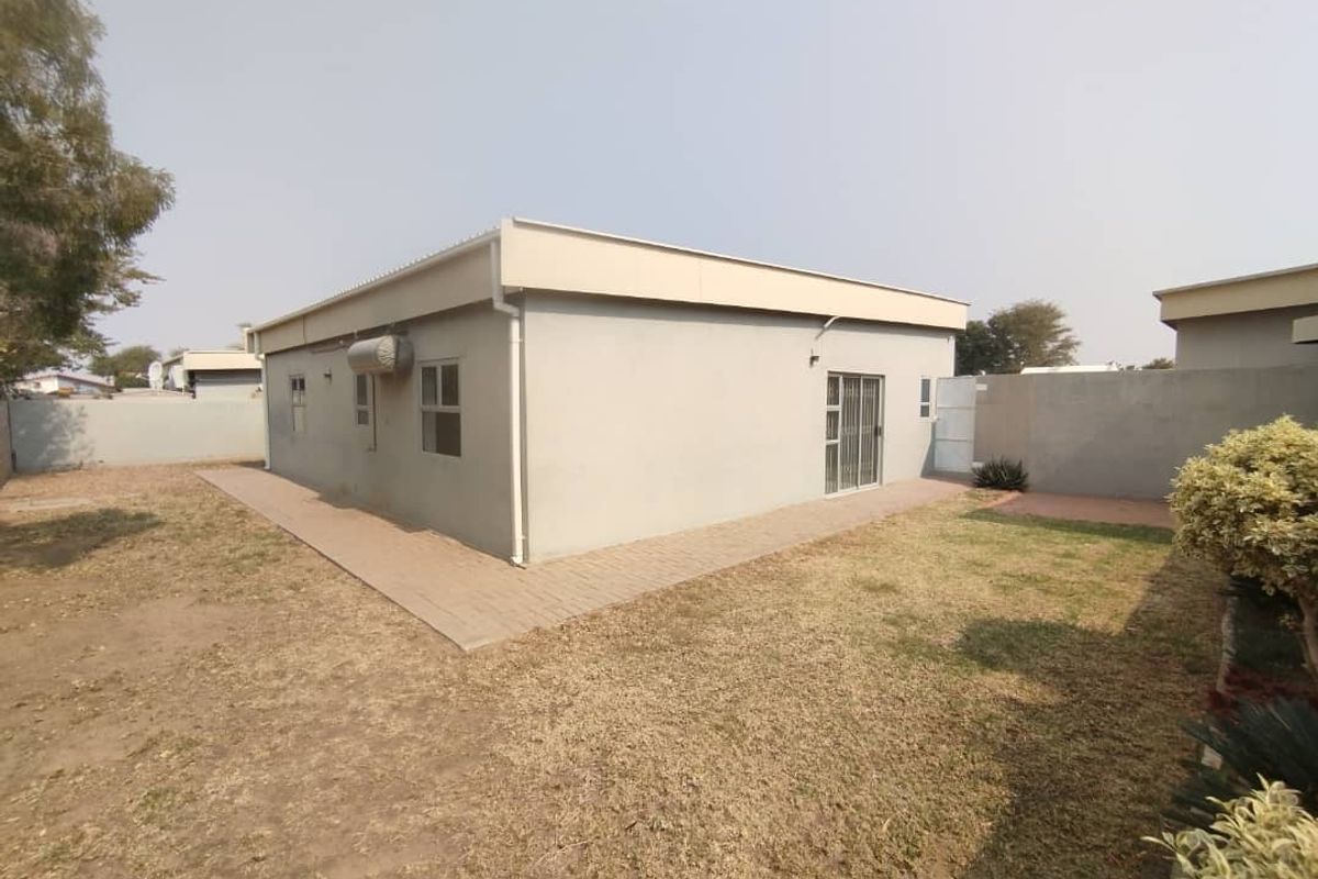 Rear view of the townhouse featuring a paved walkway, perimeter boundary wall, and a sliding glass door leading to the garden area.