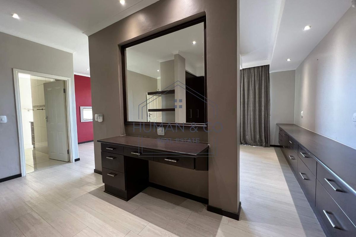 Spacious bedroom featuring built-in cabinetry, a dedicated vanity area with a large mirror, and recessed ceiling lighting.