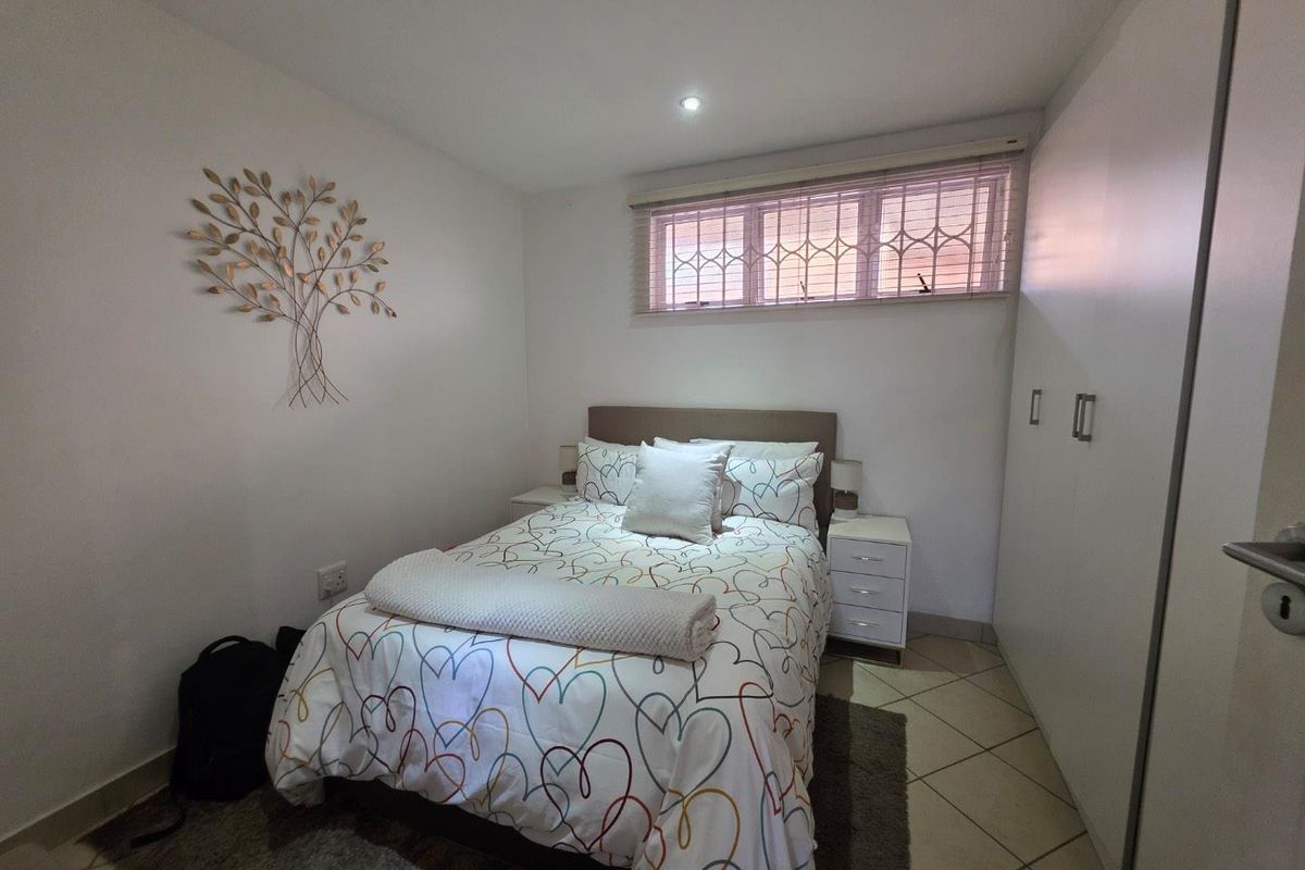 A neat bedroom featuring built-in cupboards, tiled flooring, and a window fitted with security bars.