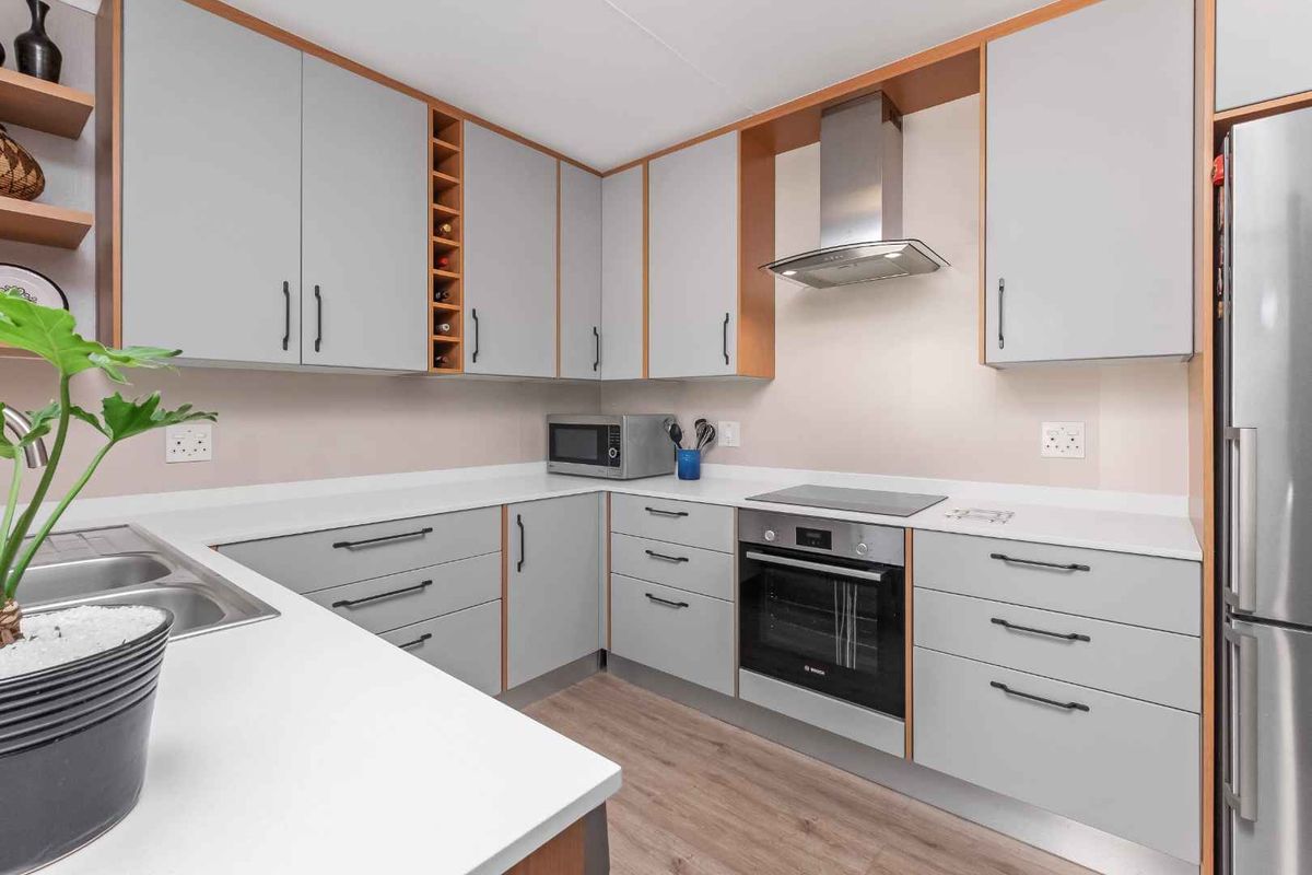 Modern kitchen featuring light grey cabinetry, stone countertops, stainless steel appliances, and durable laminate flooring.