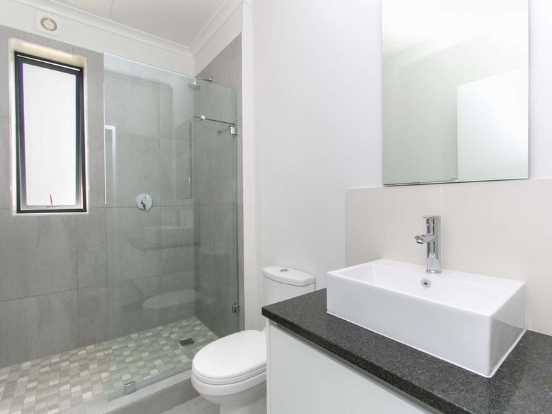 Modern bathroom featuring a glass-enclosed shower with mosaic tiling, a sleek vessel sink on a stone countertop, and a wall-mounted mirror.