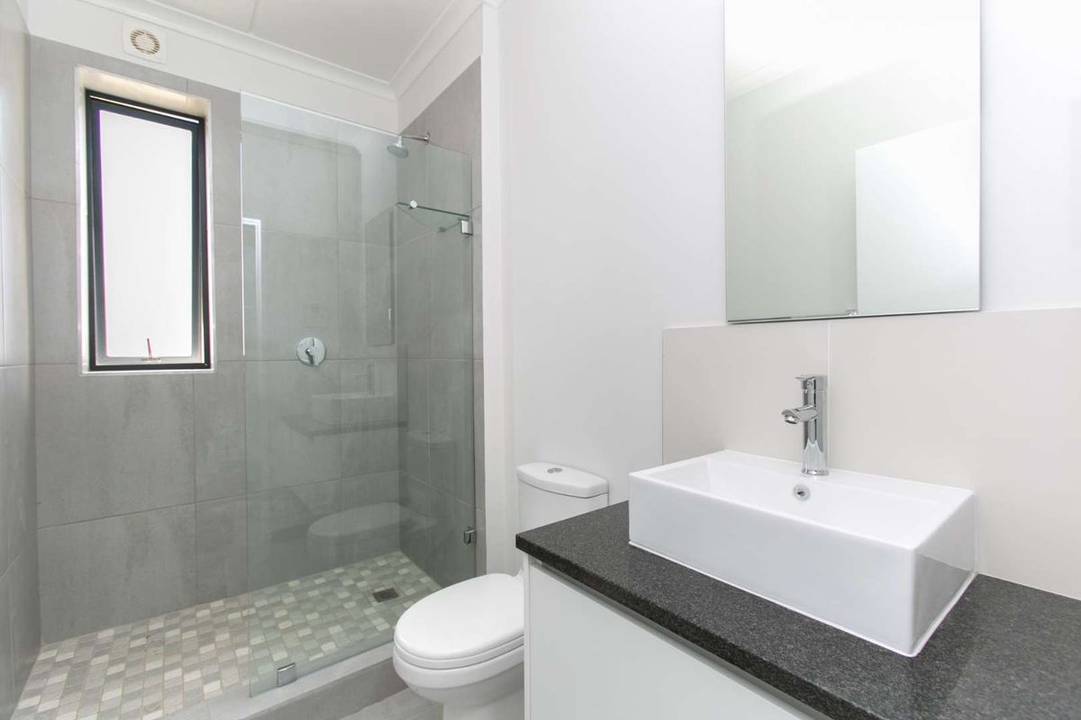Modern bathroom featuring a glass-enclosed shower with mosaic tiling, a sleek vessel sink on a stone countertop, and a wall-mounted mirror.