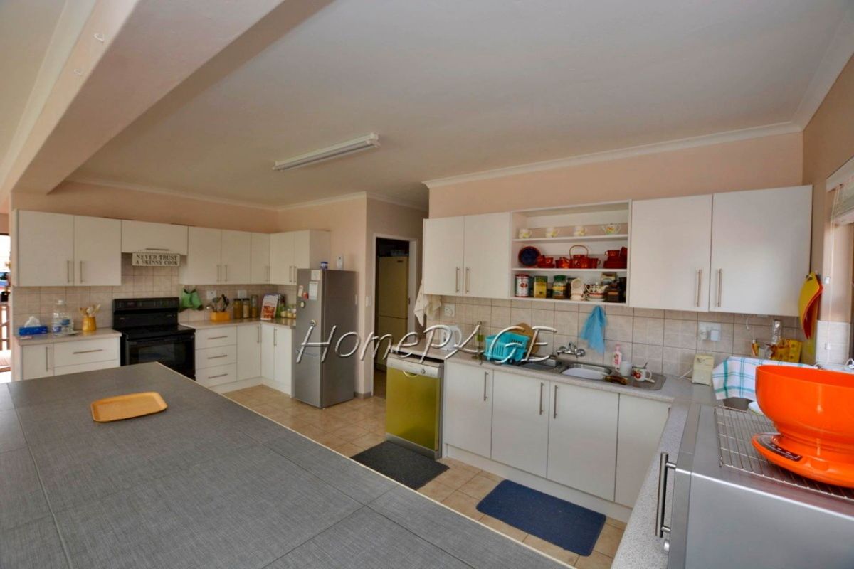 Spacious kitchen featuring white cabinetry, tiled backsplash, integrated sink, and a large central island with ample counter space.