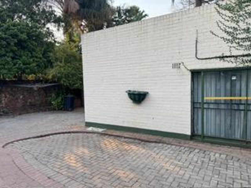 Exterior view of the property featuring a paved driveway area, painted brick facade, and a sliding glass door with security gate.