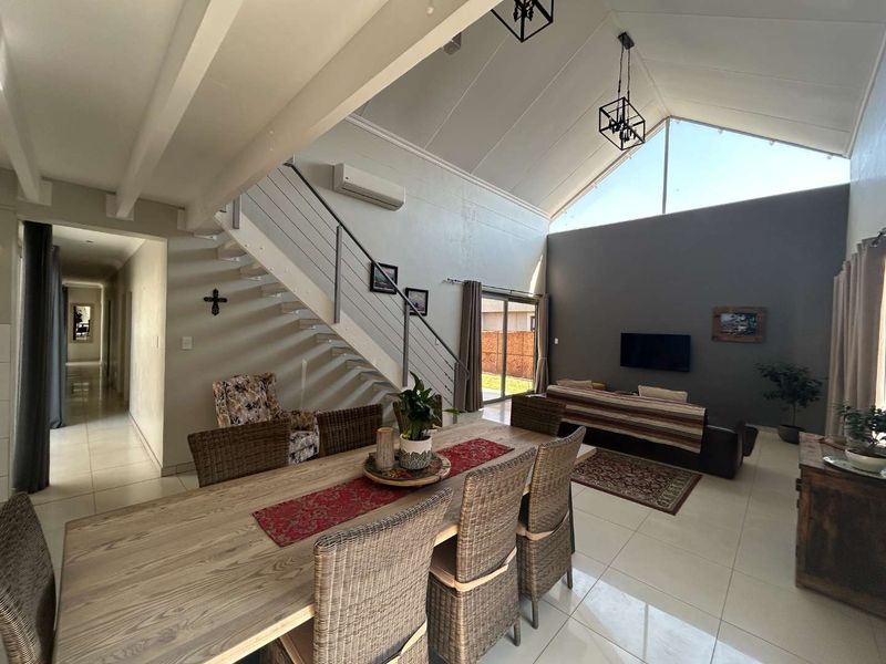 Spacious open-plan living and dining area featuring a dramatic vaulted ceiling, large feature window, tiled floors, and a modern staircase with metal balustrades.