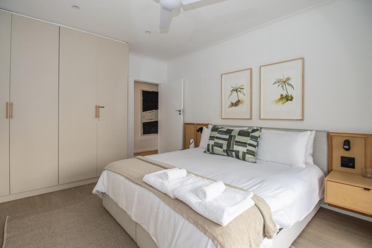 A well-maintained bedroom featuring built-in wardrobes, integrated bedside cabinetry, and a ceiling fan, finished with neutral tones and modern lighting.