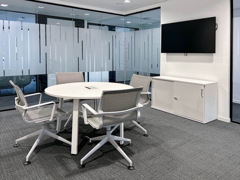 Modern office meeting room featuring glass partition walls with privacy film, carpeted flooring, and a wall-mounted television.