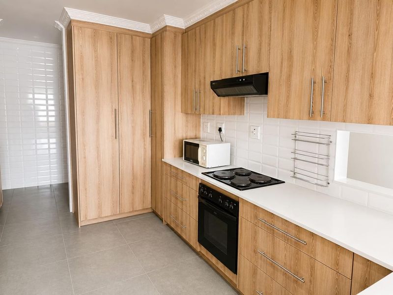 Modern kitchen featuring light wood-grain cabinetry, white subway tile backsplash, stone countertops, and integrated electric cooking appliances.
