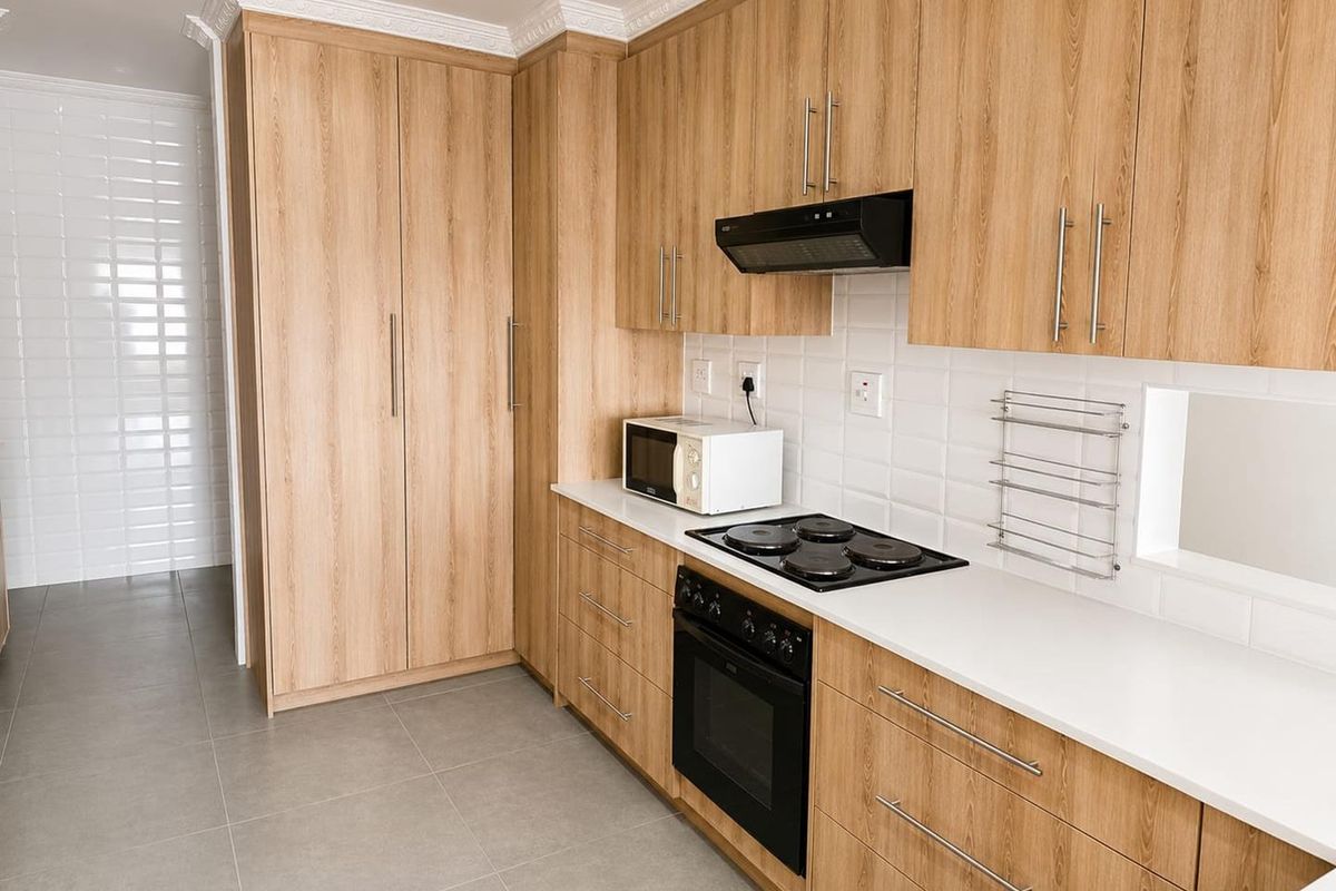 Modern kitchen featuring light wood-grain cabinetry, white subway tile backsplash, stone countertops, and integrated electric cooking appliances.