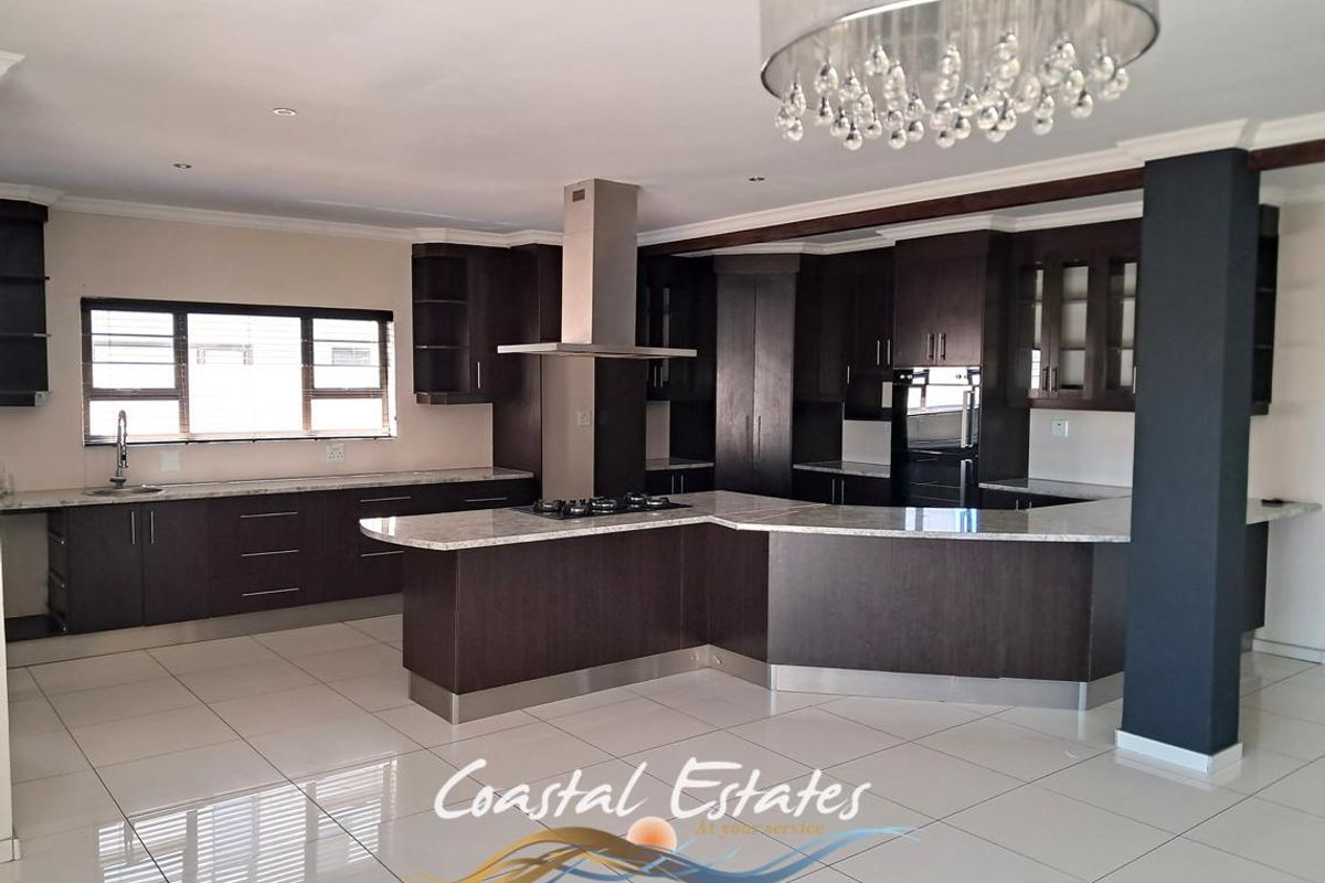 Spacious modern kitchen featuring dark wood cabinetry, stone countertops, a central island with a gas hob, and an integrated extractor fan.