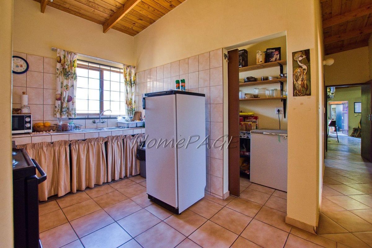 A functional kitchen featuring tiled flooring, wooden beamed ceiling, built-in sink, and an adjacent scullery area with open shelving.