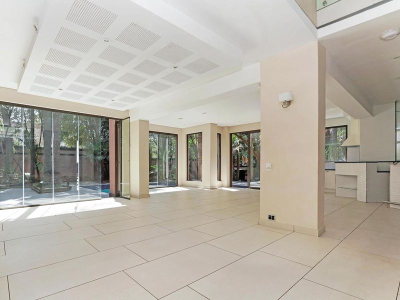 Spacious open-plan living area featuring large format floor tiles, recessed ceiling details, and expansive glass doors opening to the garden and pool area.
