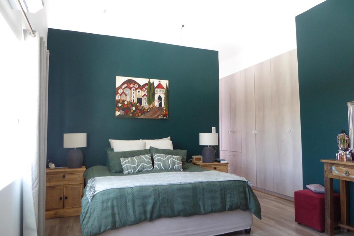 Spacious bedroom featuring dark accent wall, light wood-tone built-in cupboards, laminate flooring, and an integrated air conditioning unit.