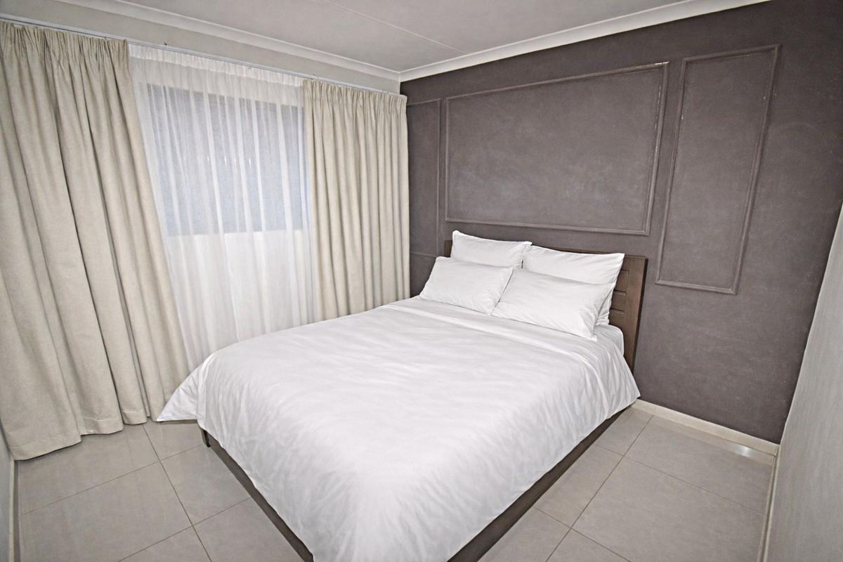 A well-maintained bedroom featuring tiled flooring, a decorative feature wall with molding, and floor-to-ceiling curtains.