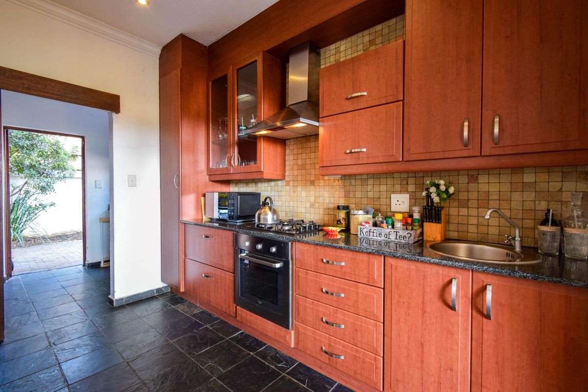 A functional kitchen featuring warm-toned wooden cabinetry, granite countertops, a built-in oven, gas hob, stainless steel extractor fan, and dark slate floor tiles.
